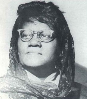 Black and white photo of Ella Little Collins in 1954, her head titled slightly upward, wearing a head scarf and glasses.