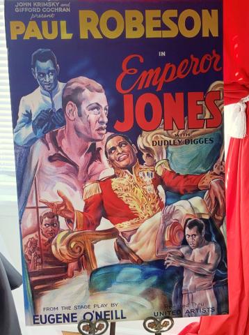 A colorful poster advertises the 1933 film Emperor Jones. The poster displays five images of Robeson at the various stages of his character’s rise as a corrupt dictator. Four of the images revolve around Robson dressed in a red and gold military uniform, with gold shoulder epaulettes evocative of the era of Napoleon Bonaparte.