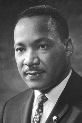 Photo portrait of Dr. Martin Luther King Jr, attired in dark suit jacket, cross-hatched tie, and white shirt.