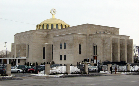 Contemporary color photo. Winter scene with snow. A gold-colored dome with high arched windows above a large granite building enclosed by a fence, with a parking lot inside the gates.