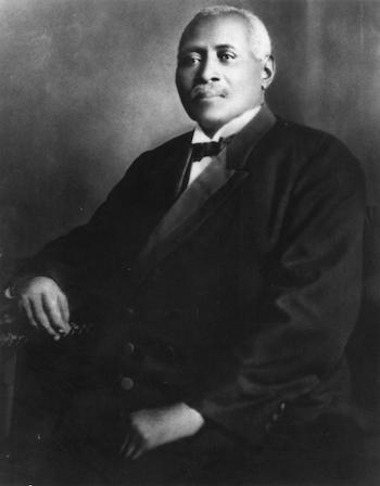 Black and white photo portrait of grey-haired Reverend William Drew Robeson, Paul Robeson’s father (1844- 1918). He wears a dark suit, white shirt, and dark bowtie; he is seated facing the camera.