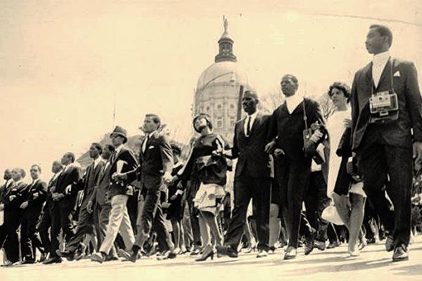 Sepia-tone photo showing a line of Black funeral marchers walking downhill past the Georgia Capitol building. The Capitol’s dome appears in the background.