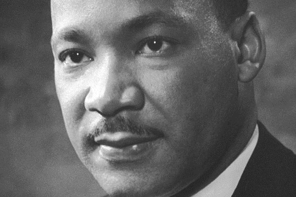 Photo portrait of Dr. Martin Luther King Jr, attired in dark suit jacket, cross-hatched tie, and white shirt.