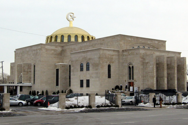 Contemporary color photo. Winter scene with snow. A gold-colored dome with high arched windows above a large granite building enclosed by a fence, with a parking lot inside the gates.