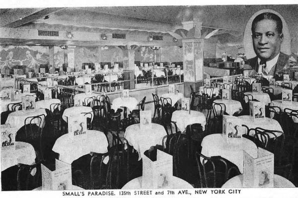 Black and white postcard of the Paradise Room, likely printed in the 1930s. Numerous tables, each with a white tablecloth, menu, and hairpin side chairs, fill up the spacious room. A photo of Ed Smalls, in coat and tie, appears in the top-right corner of the postcard.